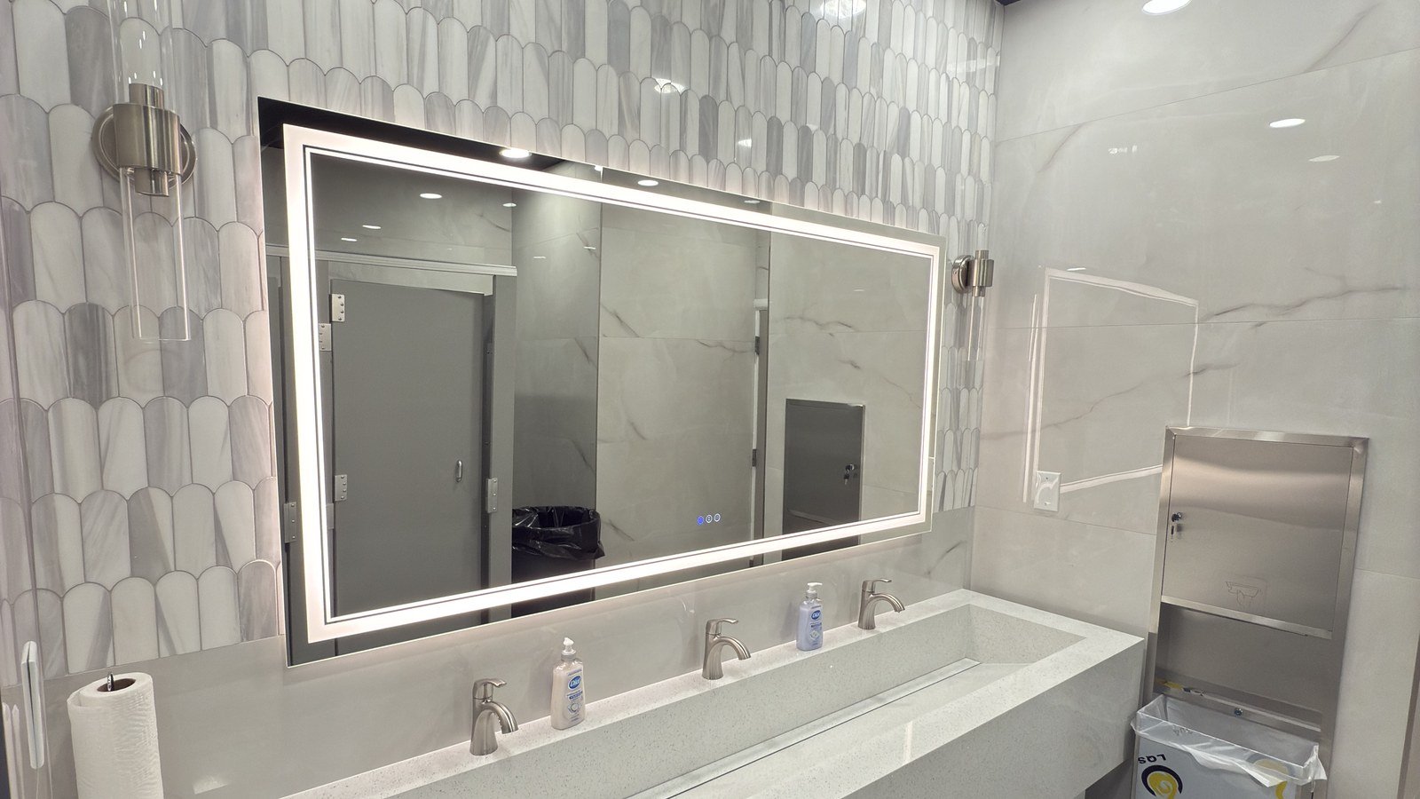 Commercial restroom renovation with trough sink and backlit mirror